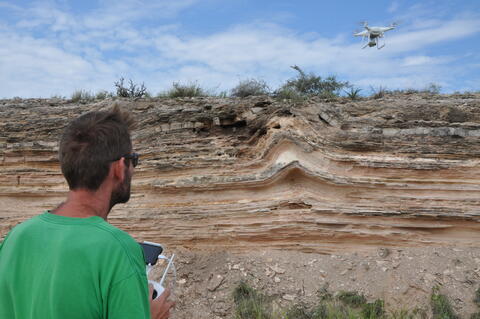 an engineer in a green shirt flying a drone over varied terrain
