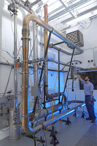 Technician standing under a two-story burner system with numerous pipes and connections