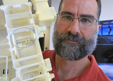 SwRI’s Dr. Thomas Greathouse uses an engineering model of the Lyman-Alpha Mapping Project (LAMP) instrument to show a failsafe door (outlined by rectangle) recently opened in lunar orbit. Located below the regular aperture door (circled), the door opened 
