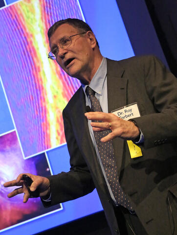 Portrait of Roy Torbert in front of a presentation screen talking to a crowd