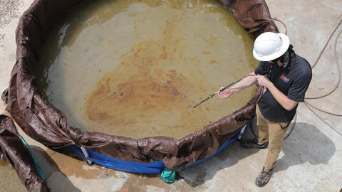 A tank with plastic lining holding water with an engineer spraying oil inside with a wand