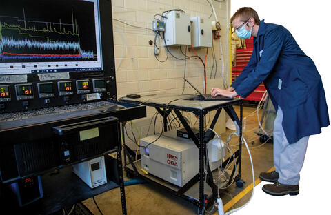 man in blue lab coat and mask working on a laptop in front of usgr
