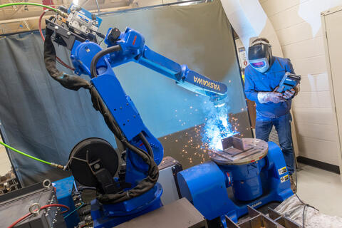Researcher wearing safety equipment, working with a welding robotic system