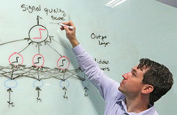 Scientist points to a white board with the process for a neural network scoring a signal quality displayed
