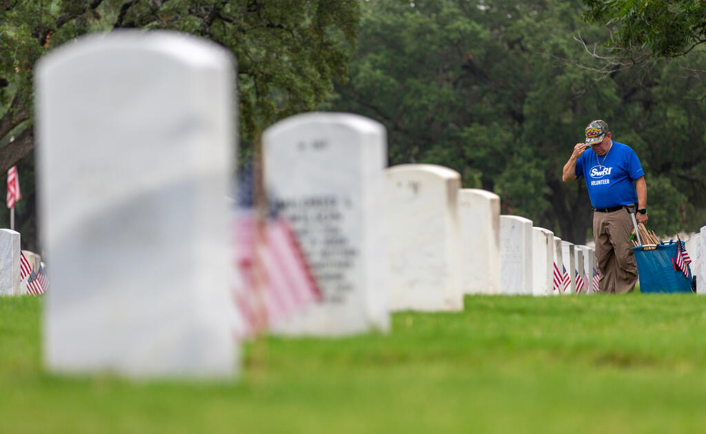 Looking down a row of tombstones with SwRI staff member in the distance placing a flag at a tombstone