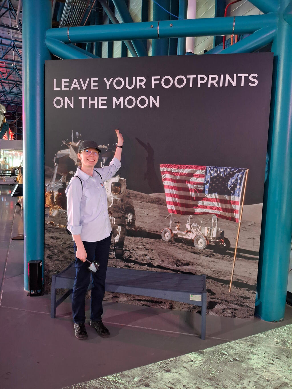Dr. Sokol in front of "Leave your Footprints on the Moon" sign and pointing her left hand towards sign