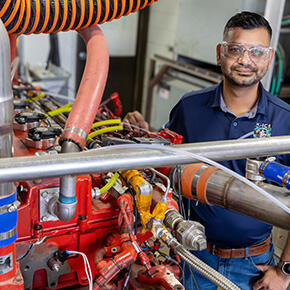 SwRI staff member posing behind a hydrogen ICE vehicle test cell in SwRI's multifuel lab