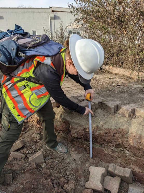 Scientist with hard hat and safety vest measures damage of cracked ground from earthquake with a tape measure.