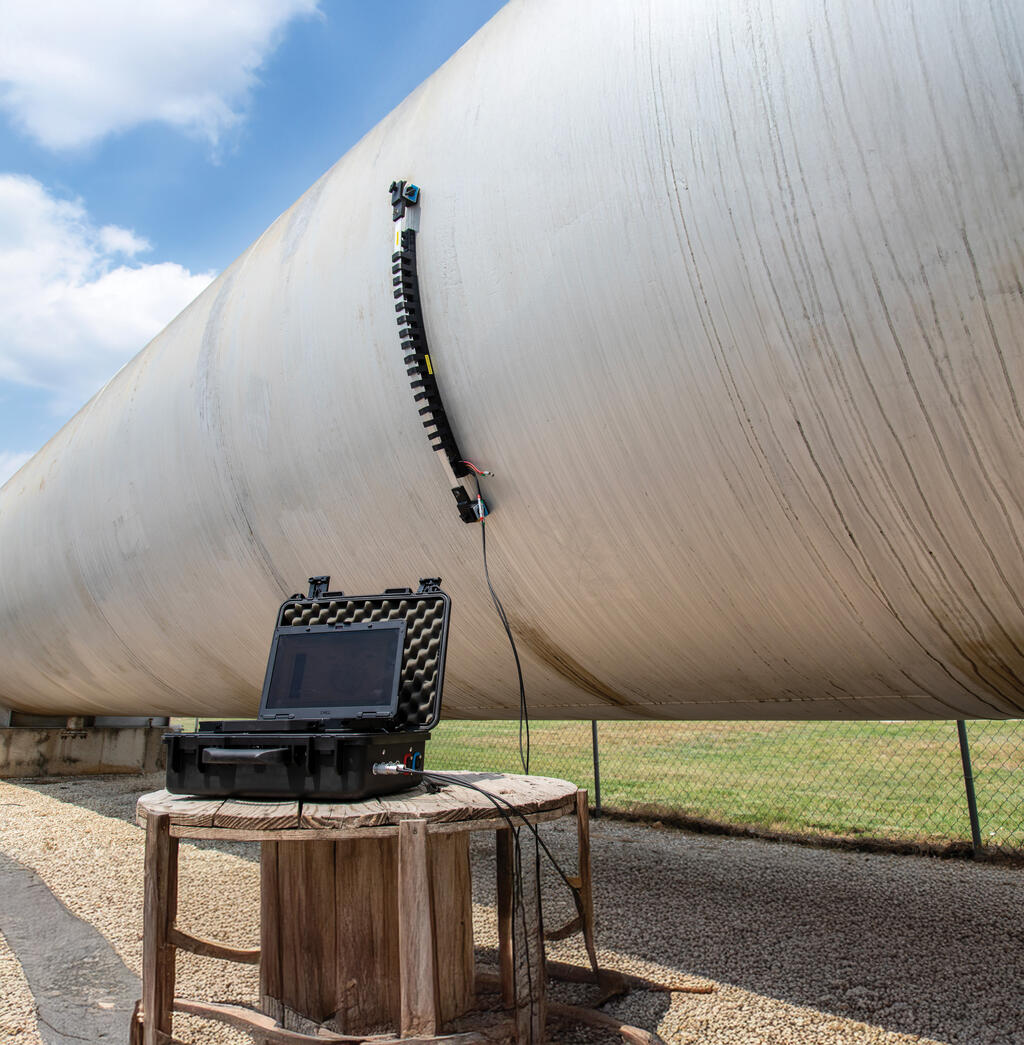 Magnetostrictive (MST) probe attached to side of storage tank with laptop connected laying on a wooden table