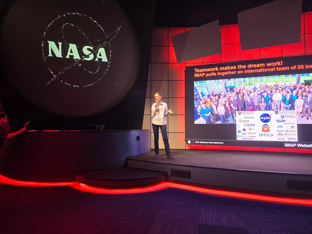 Dr. Sokol standing on stage facing audience with large screen showing presentation behind her
