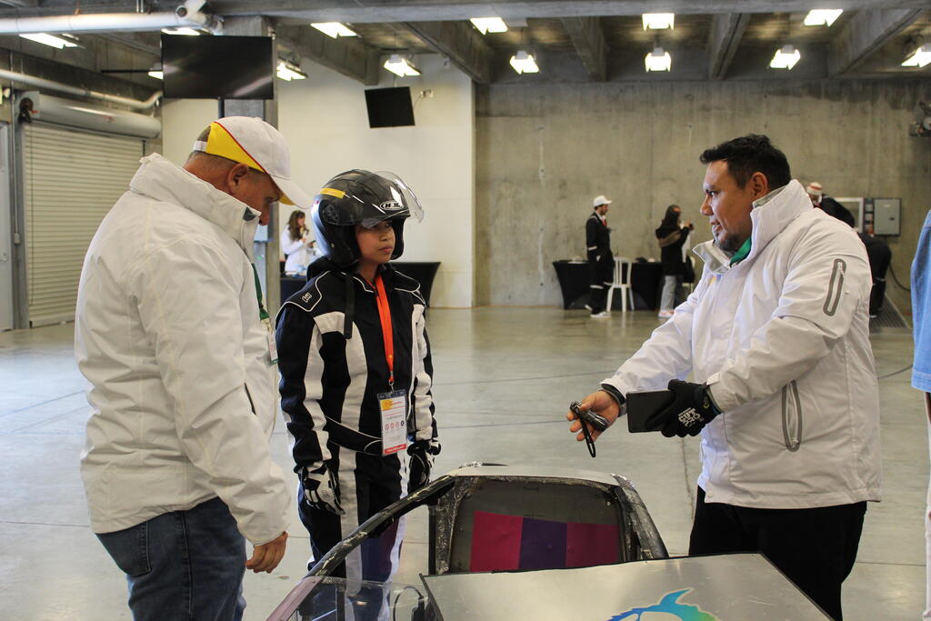 Two male SwRI staff providing technical and engineering support to student in driving gear for the Shell-Eco Marathon engineering competition