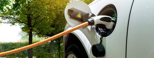 White electric car with the power cable supply plugged in to charge on a sunny day