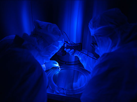 The University of New Hampshire’s Skylar Vogler (left) and SwRI’s Amanda Wester use UV light to detect and remove particles from the IMAP-Lo collimator grids and spacers.