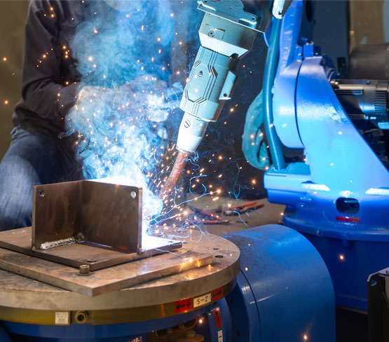 Welder demonstrates a test fixture for automated robotic welding of steel ship parts.